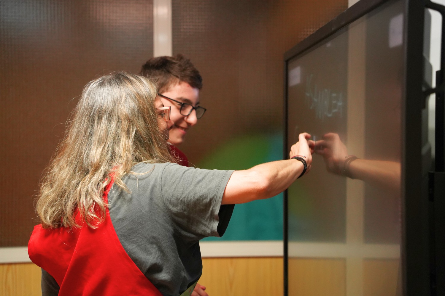 Profesora y estudiante escribiendo en la pantalla digital